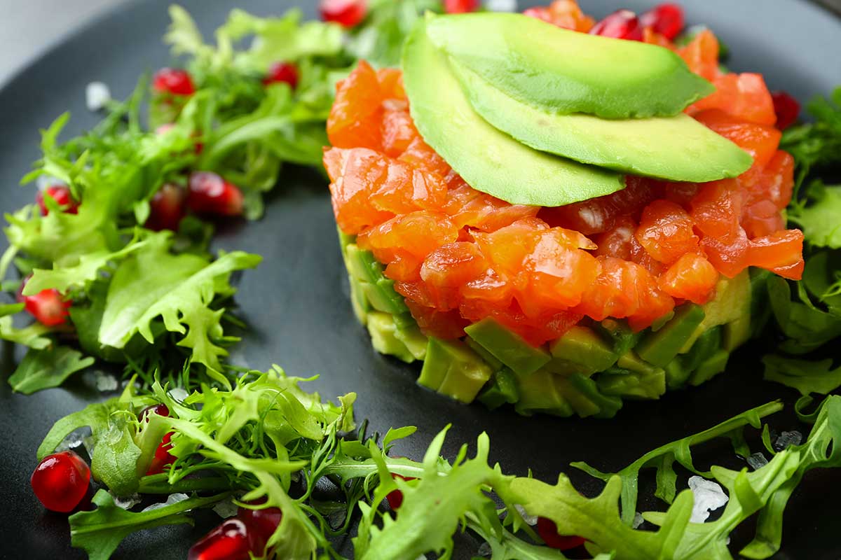 Piatto nero con tartare di salmone, avocado, rucola e melograno serviti come antipasto sfizioso