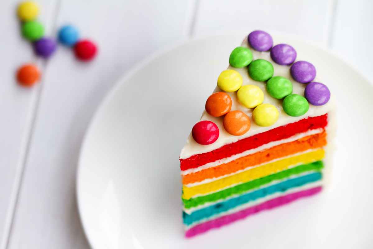 piatto bianco con fetta di torta arcobaleno per carnevale