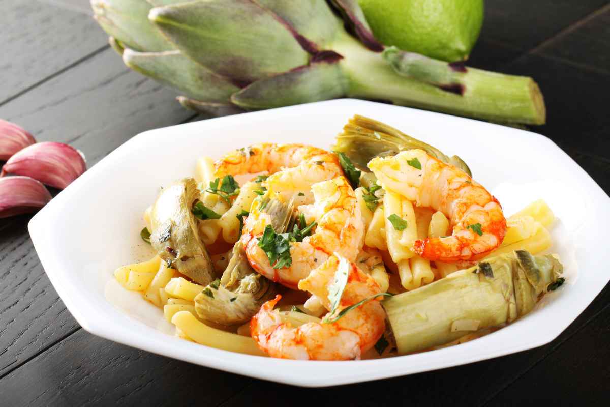 piatto di pasta corta con condimento di carciofi e gamberi