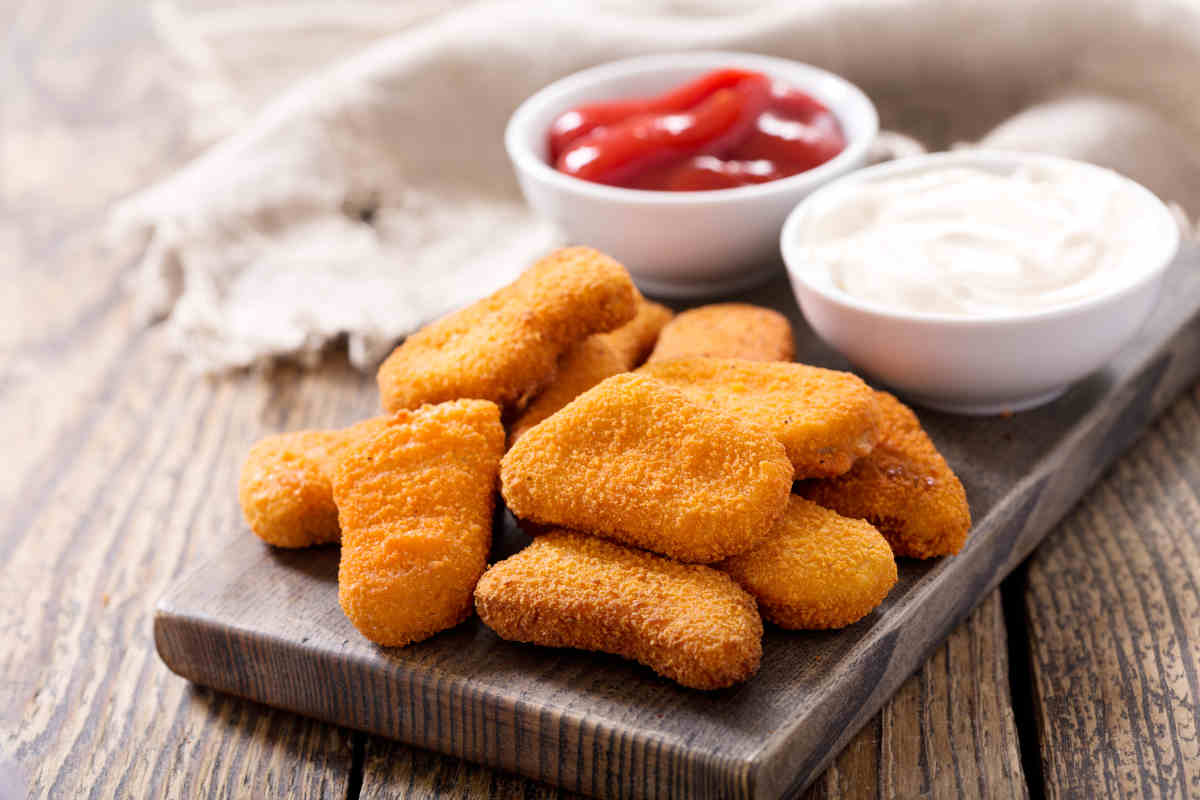 tagliere con nuggets e due ciotoline di salse rossa e bianca