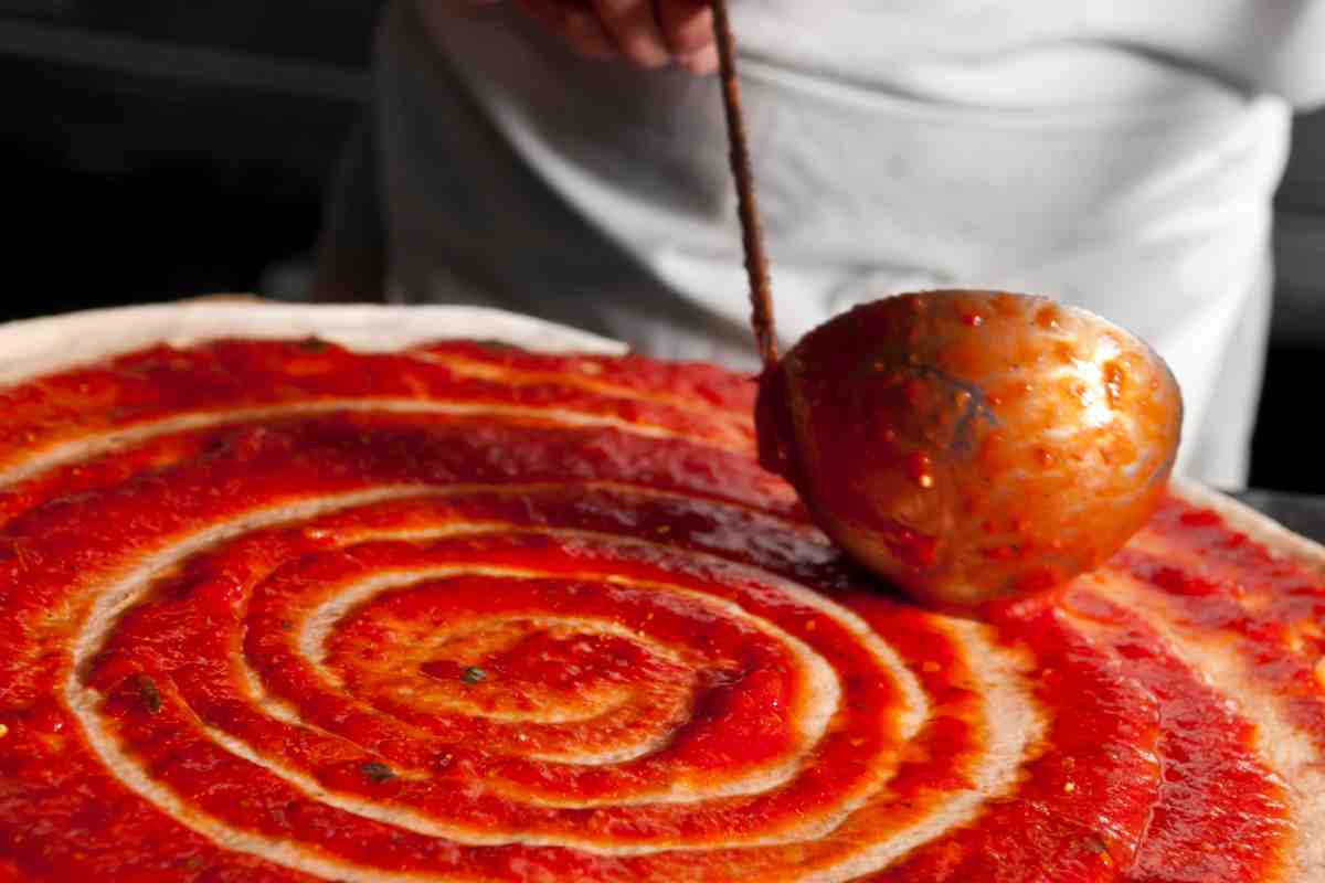 Pizzaiolo versa una delle migliori passate di pomodoro sulla pizza con un mestolo