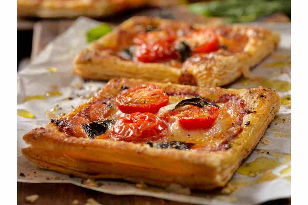 Pizzette sfoglia con pomodorini su una teglia con carta da forno