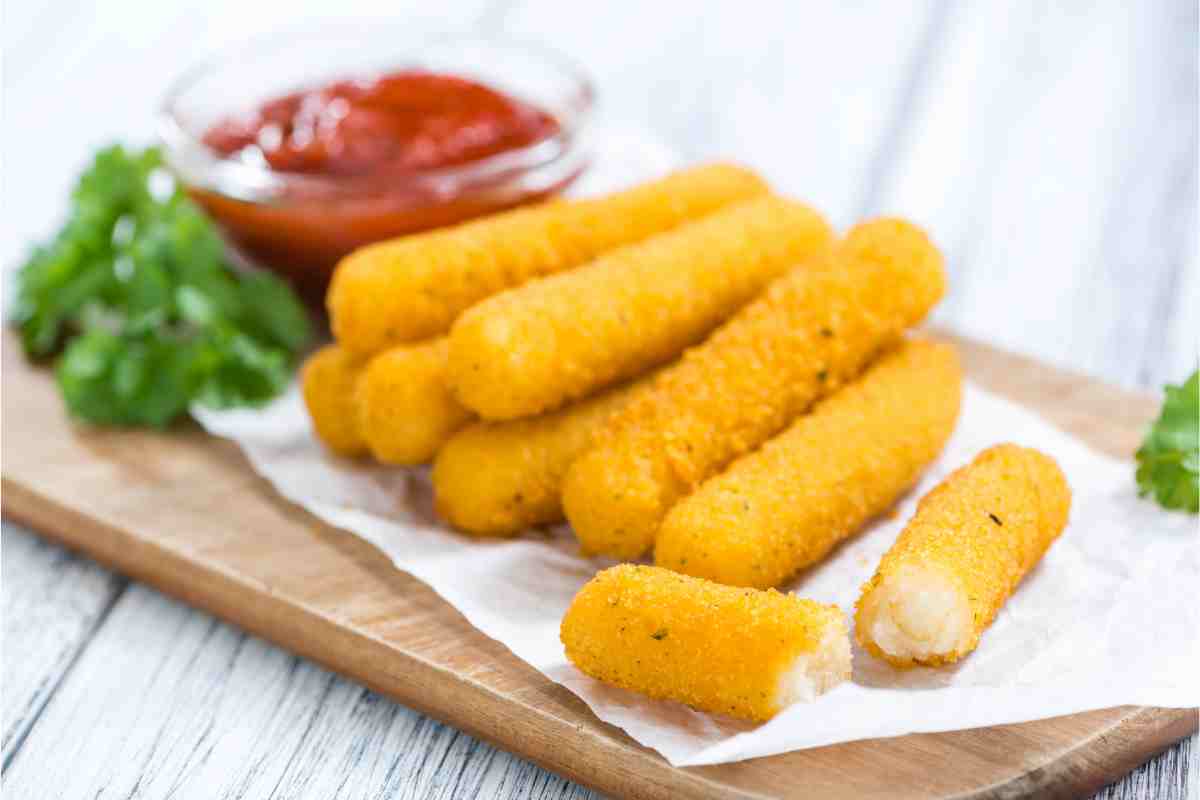 tagliere di legno con sopra una pila di bastoncini di mozzarella fritta