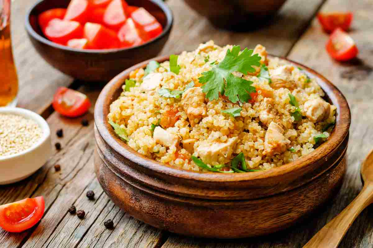 Insalata di quinoa con pollo e verdure in una terrina di coccio su tavola di legno