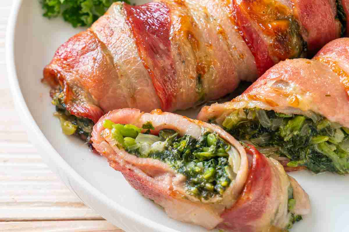 piatto bianco contenente involtini di pancetta e spinaci interi e tagliati