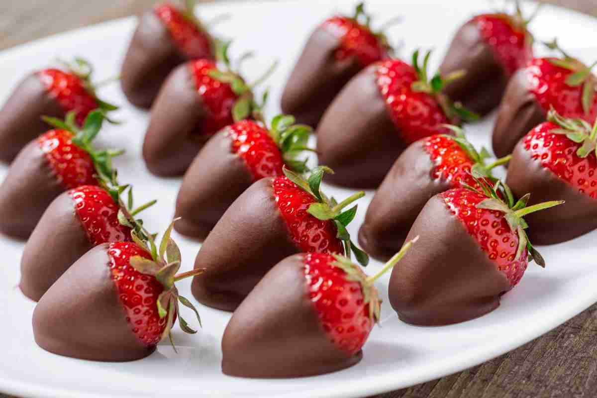 Fragole al cioccolato al latte messe in fila su un piatto bianco