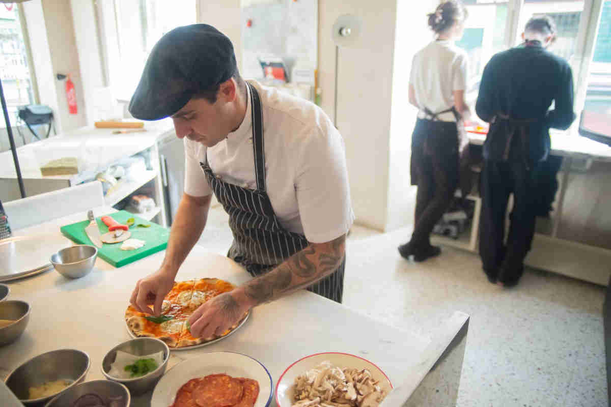 pizzaiolo che sta preparando una pizza nella cucina di una pizzeria