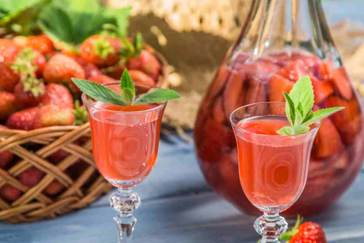 Fragolino liquore alle fragole fatto in casa in due bicchieri con la frutta in un cesto sullo sfondo