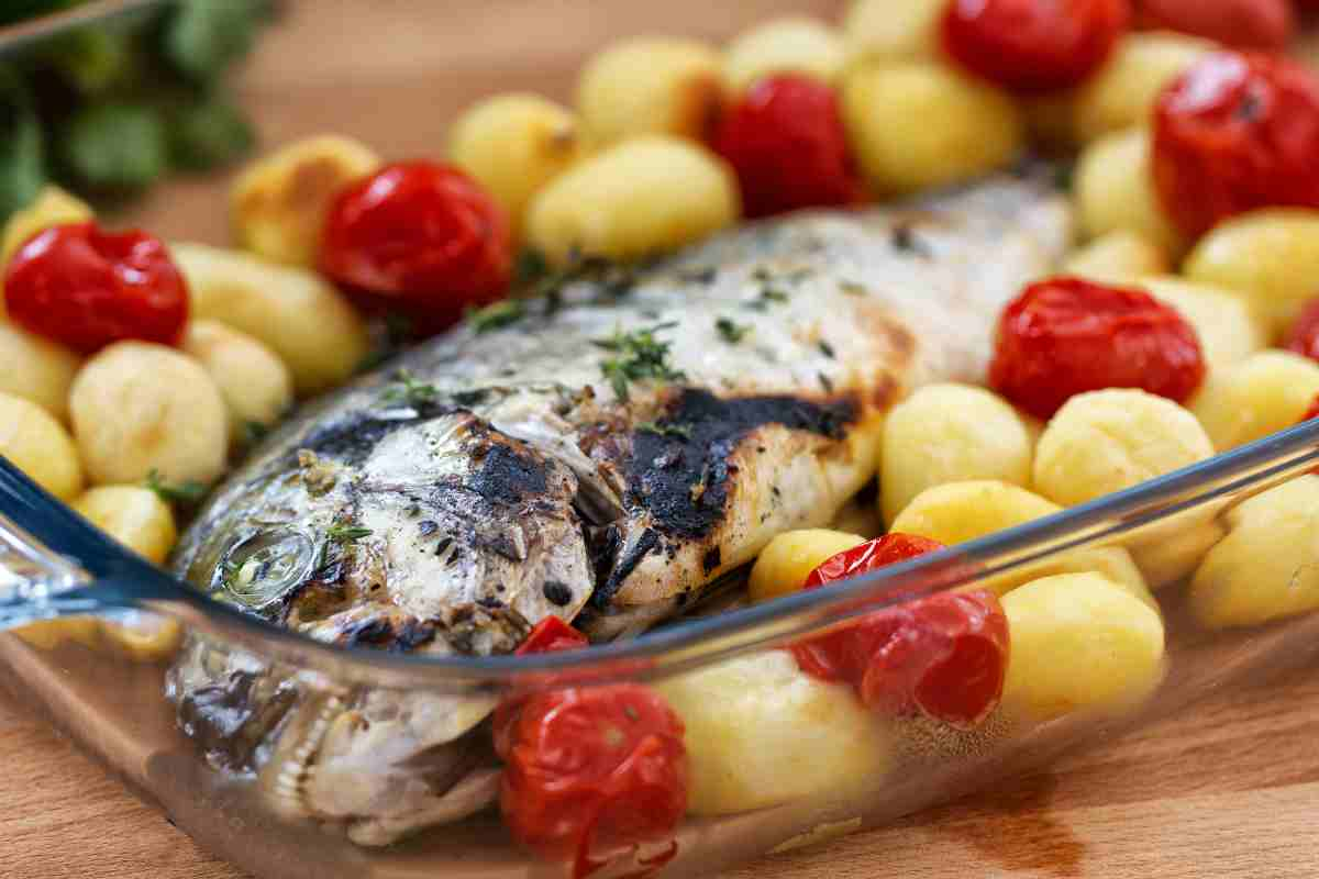 Orata al forno alla ligure in una pirofila con pomodorini e patate