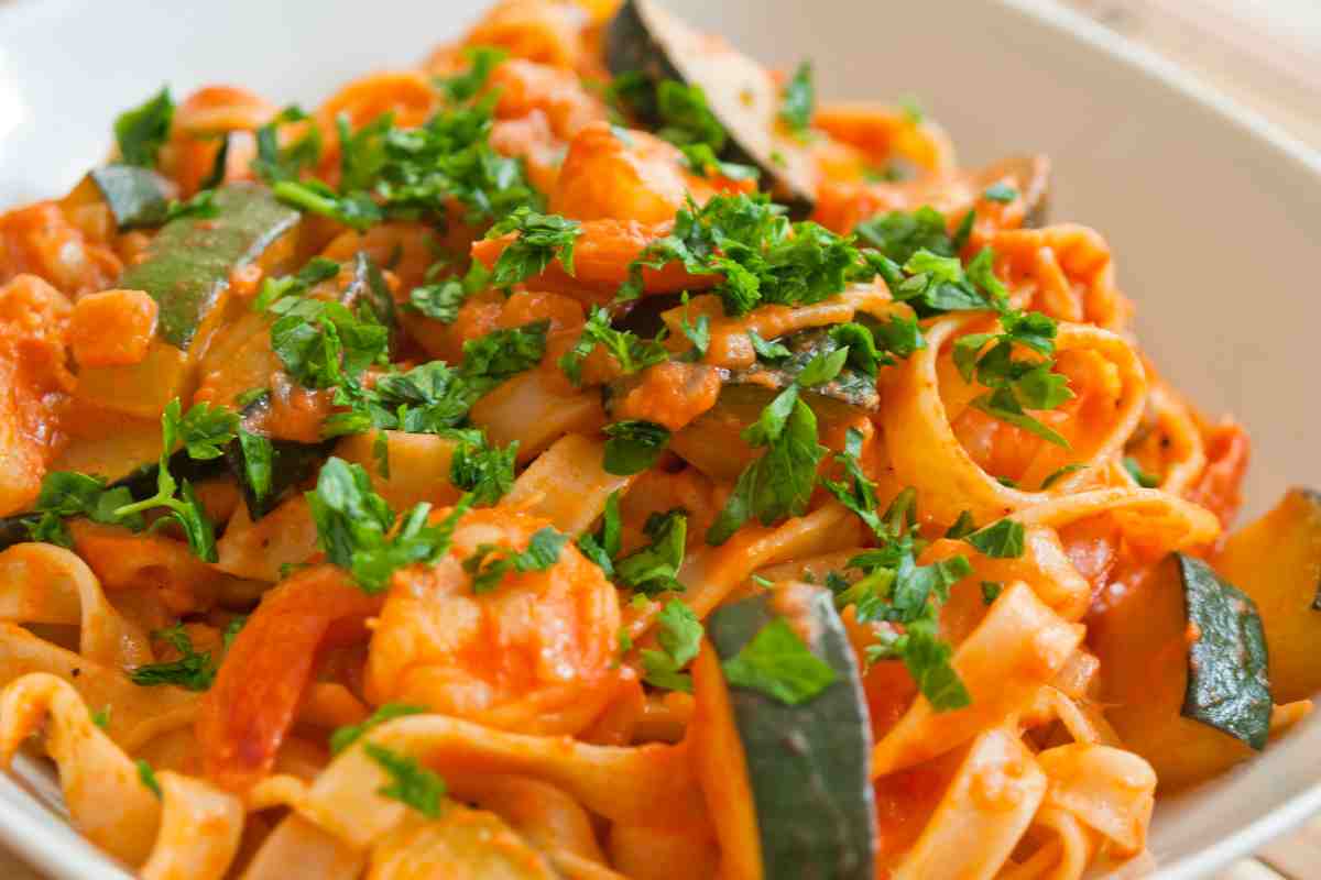 Tagliatelle gamberi e zucchine spolverate con prezzemolo in un piatto bianco