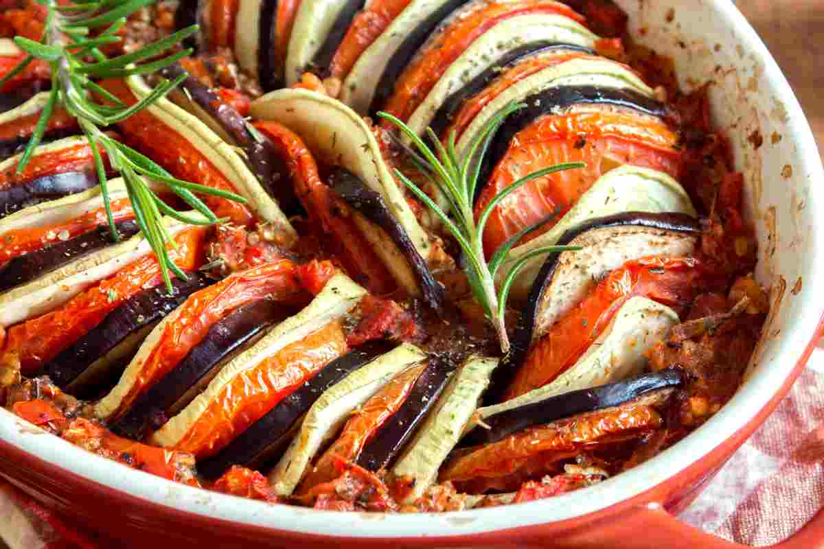 Ratatouille estiva con rametti di rosmarino sopra in una pirofila rossa